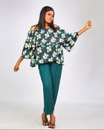 Woman wearing a floral off-shoulder top and teal pants on a white background